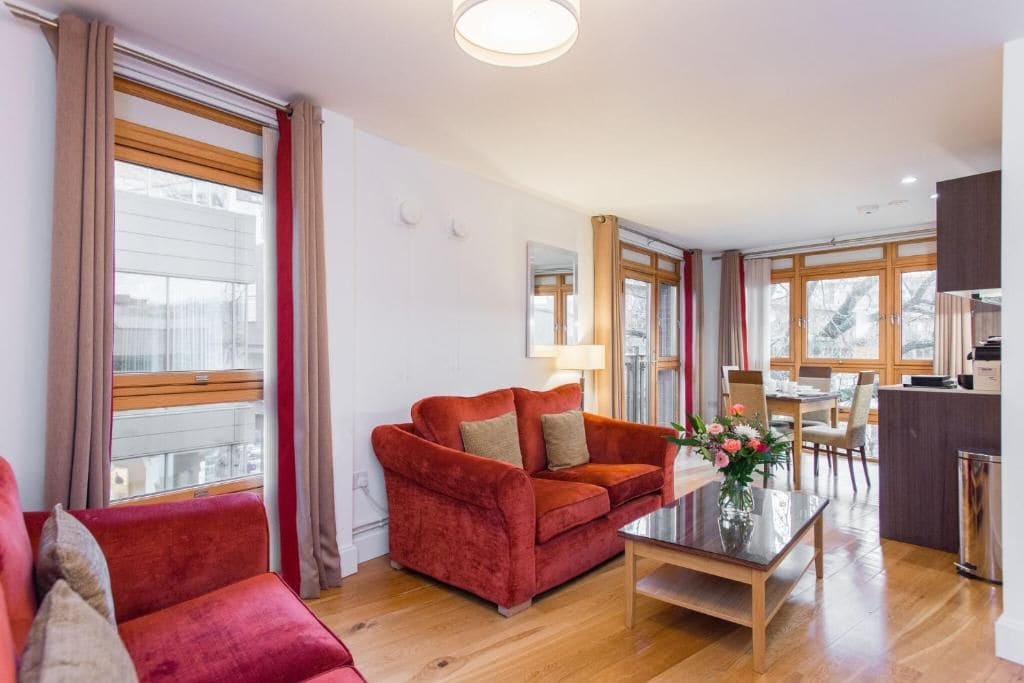 Ett modernt vardagsrum med en röd soffa, ett soffbord i glas och en matplats med ett bord och stolar i trä.