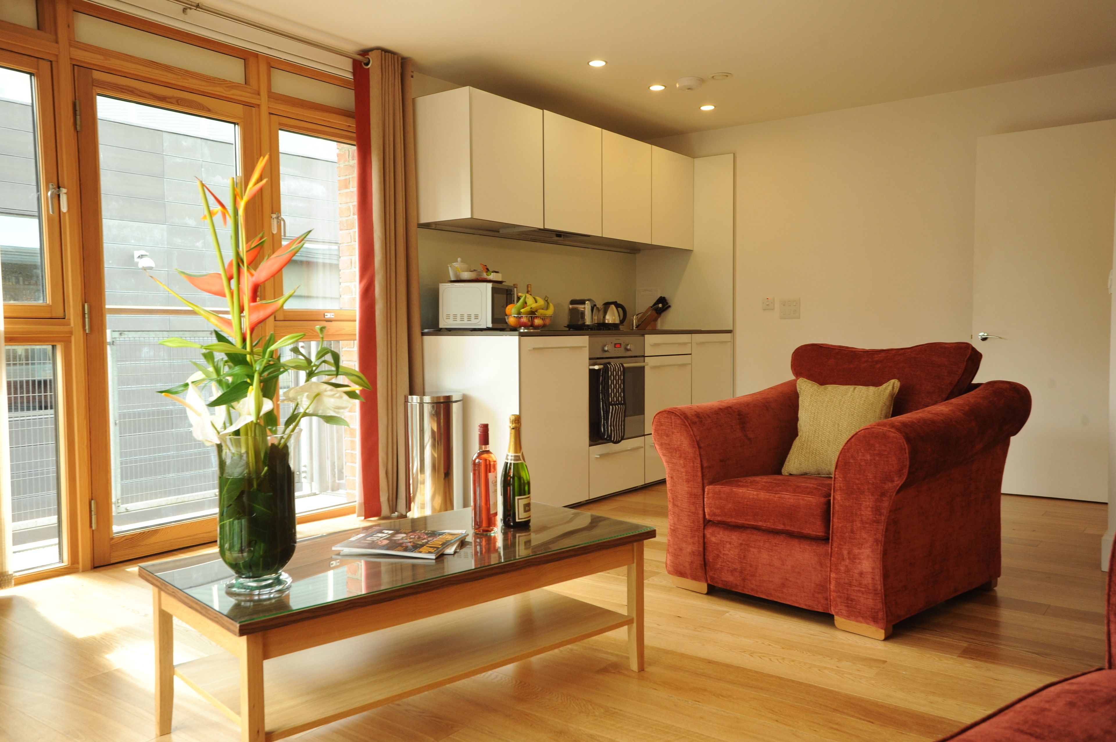 A modern living room with a glass coffee table, a red armchair, and a vase with flowers.