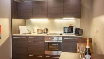 A modern kitchen with dark cabinetry, a built-in oven, a microwave, and a dining area with a bottle of champagne.