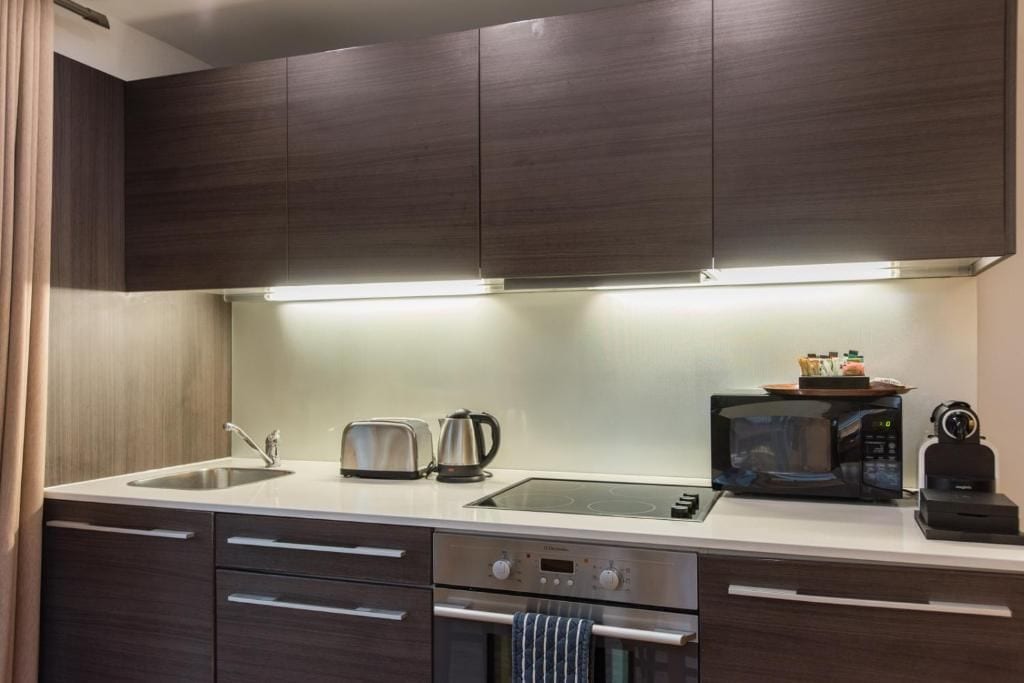 A modern kitchen with dark wood cabinets, a stainless steel sink, a toaster, a kettle, a microwave, and a built-in oven.