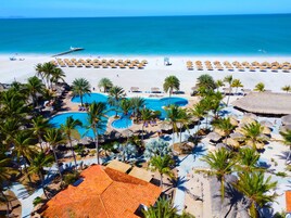 A resort with multiple swimming pools, palm trees, and a beach area.