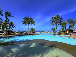 A pool area with lounge chairs, palm trees, and a view of the beach.