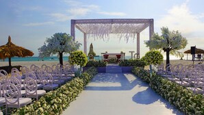 A beach wedding setup with a white aisle, white chairs, and floral decorations. - Sunsol Punta Blanca (San Pedro)
