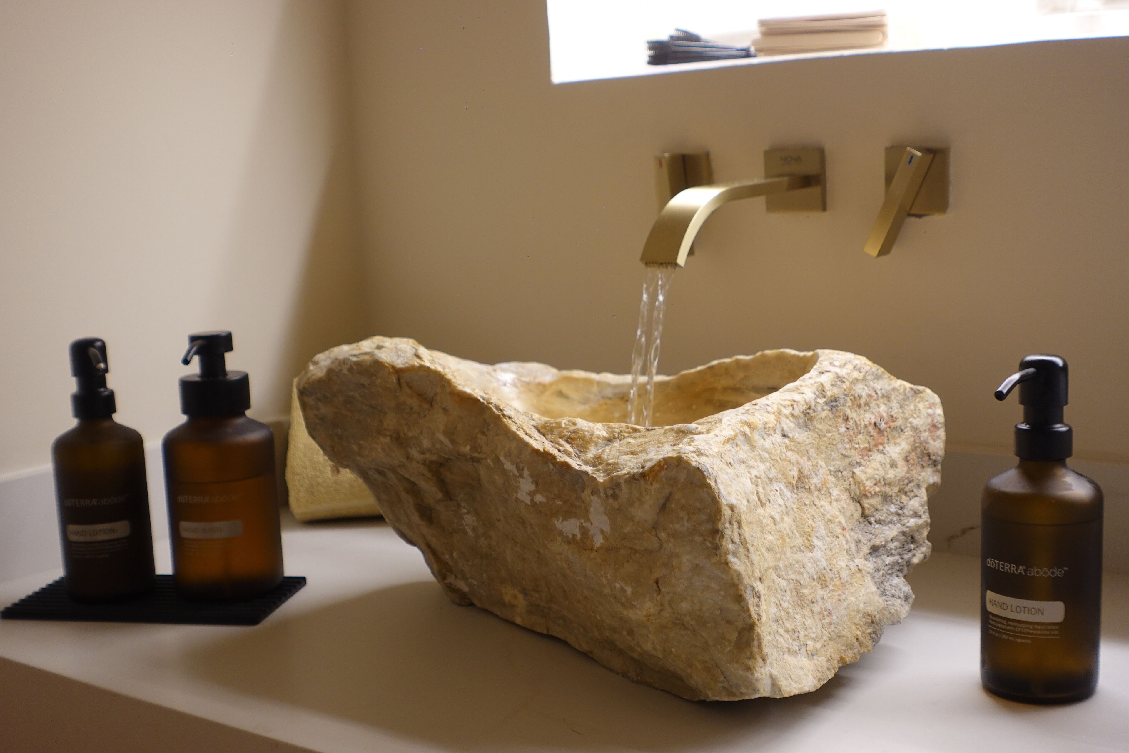 Un évier en pierre avec un robinet moderne, deux flacons de lotion pour les mains et une fenêtre en arrière-plan.