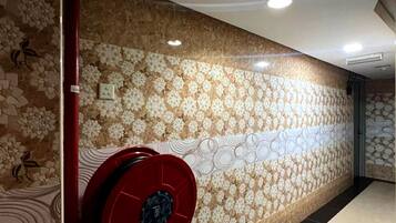 Um corredor com ladrilhos estampados na parede, um alarme de incêndio vermelho e piso ladrilhado.