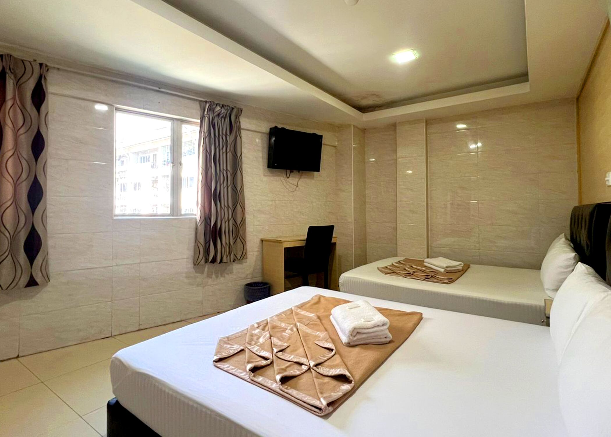 Habitación de hotel con dos camas, un televisor de pantalla plana montado en la pared y una ventana con cortinas.