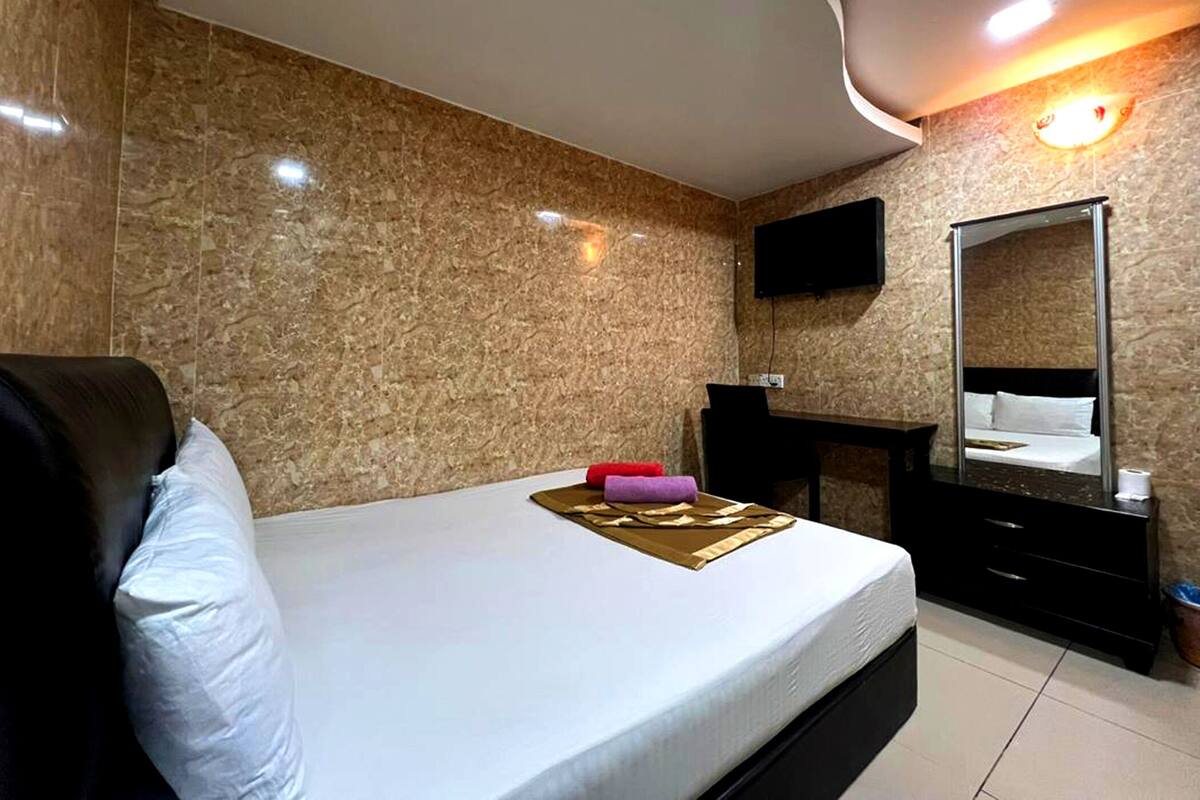 Une chambre d’hôtel comprenant un lit, un bureau, une chaise, un téléviseur à écran plat fixé au mur et un grand miroir.