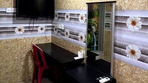 Ein kleiner Raum mit einem schwarzen Schreibtisch, einem roten Sessel, einem Spiegel und einem wandmontierten Fernseher.