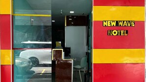Der Eingang zum New Wave Hotel mit Glastür, einem Empfangstresen im Inneren und einem rot-gelben Farbschema an den Wänden.