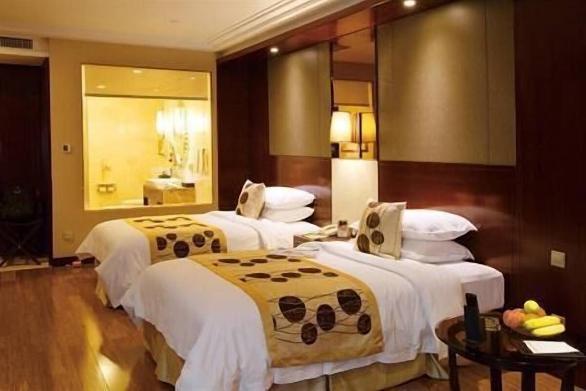 A hotel room with two beds, a small table with fruit, and a mirror.
