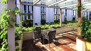 Un invernadero con terraza de madera, sillas y plantas en macetas.