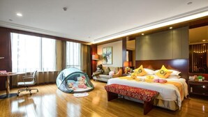 Habitación de hotel con una cama grande, un escritorio, una silla, un pequeño espacio tipo tienda para jugar y un amplio ventanal.