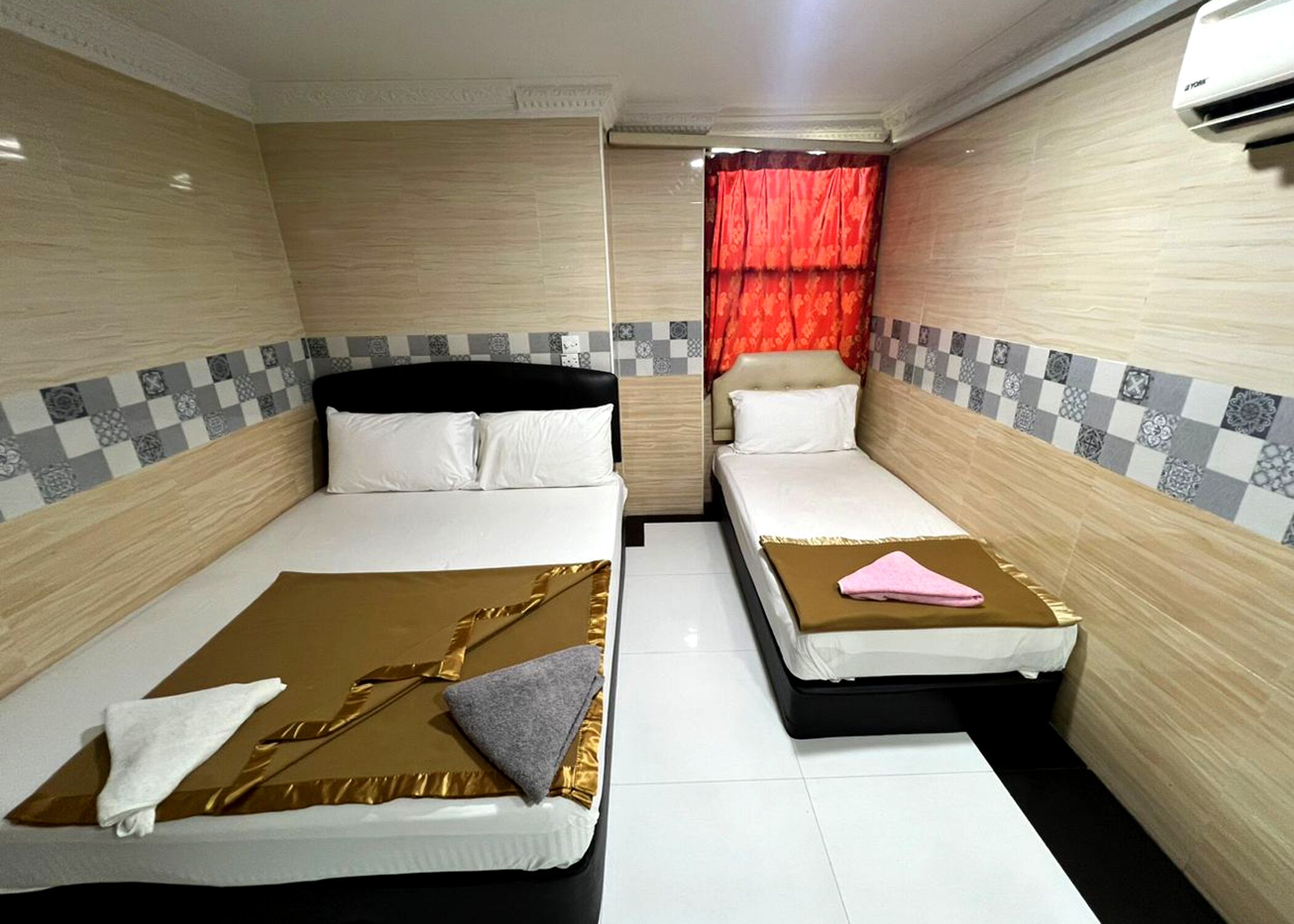 Une chambre d’hôtel avec deux lits simples, un rideau rouge et un appareil de climatisation blanc.
