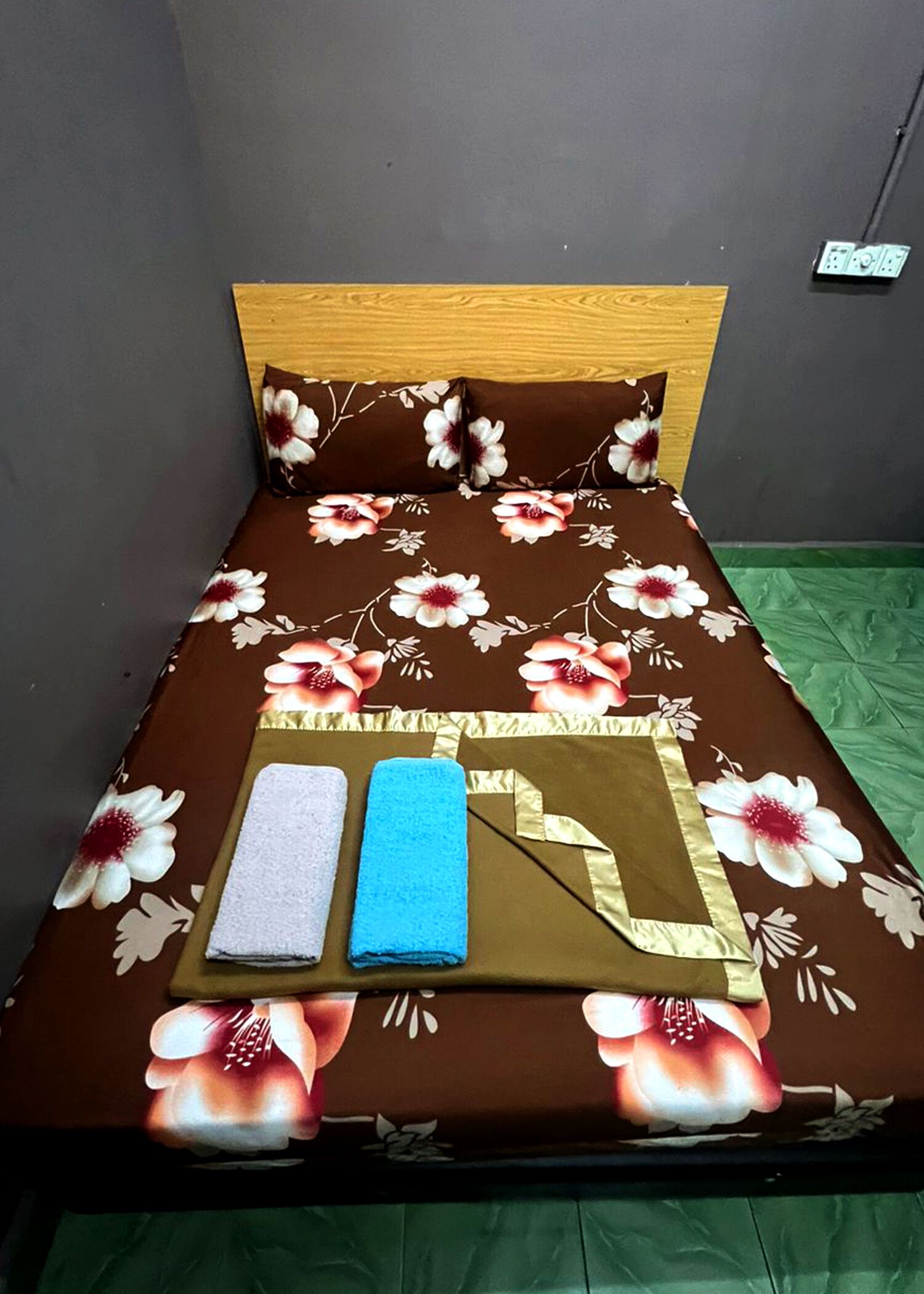 A bed with a floral bedspread, two towels, and a green blanket.