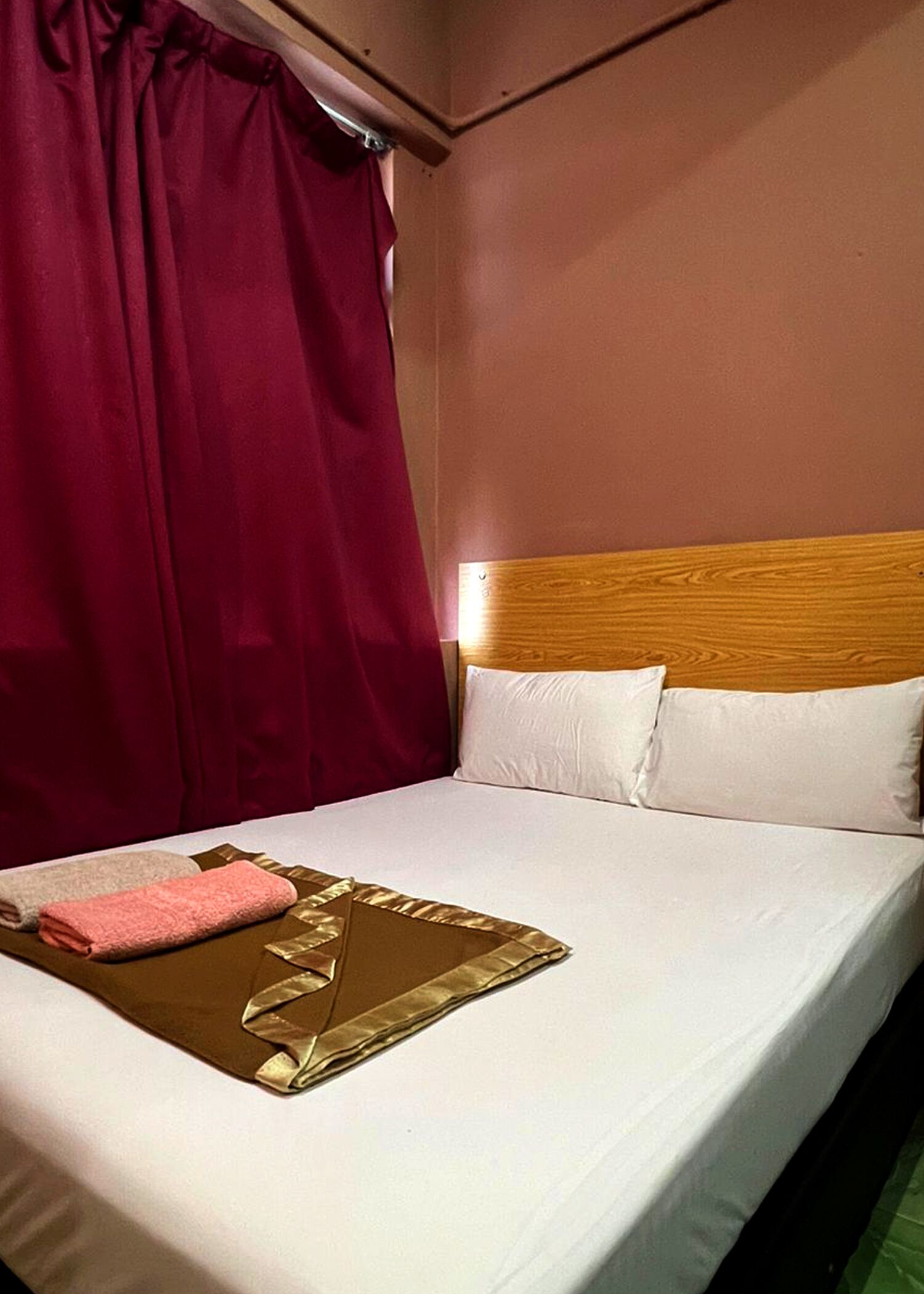 Una cama bien hecha con sábanas blancas, un cabecero de madera y una toalla rosa.