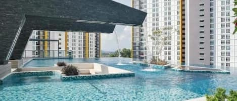 Un hotel moderno con una amplia piscina exterior, edificios altos al fondo y una estructura negra distintiva en primer plano.