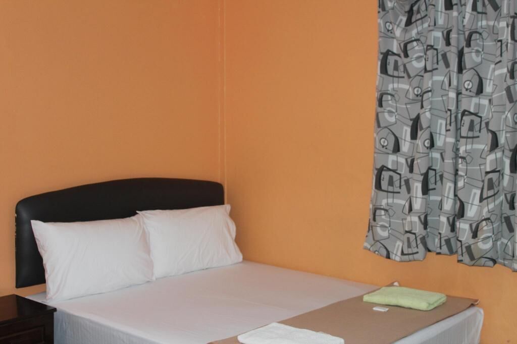 A hotel room with a bed, a nightstand, and a curtain with a pattern.