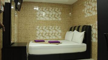 A hotel room with a bed, a TV, and a wall with a floral pattern.