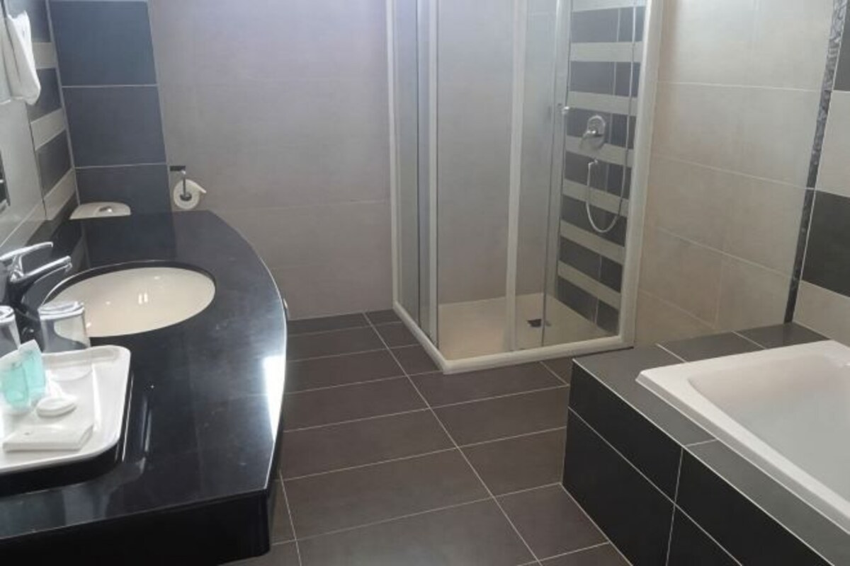 A bathroom with a black countertop sink, a glass shower enclosure, and a bathtub.