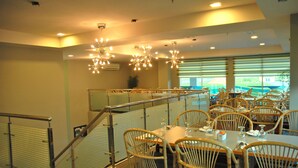 A restaurant with wicker chairs, tables set with wine glasses, and a staircase with a metal railing. - The Pavilion Hotel (Sandakan)