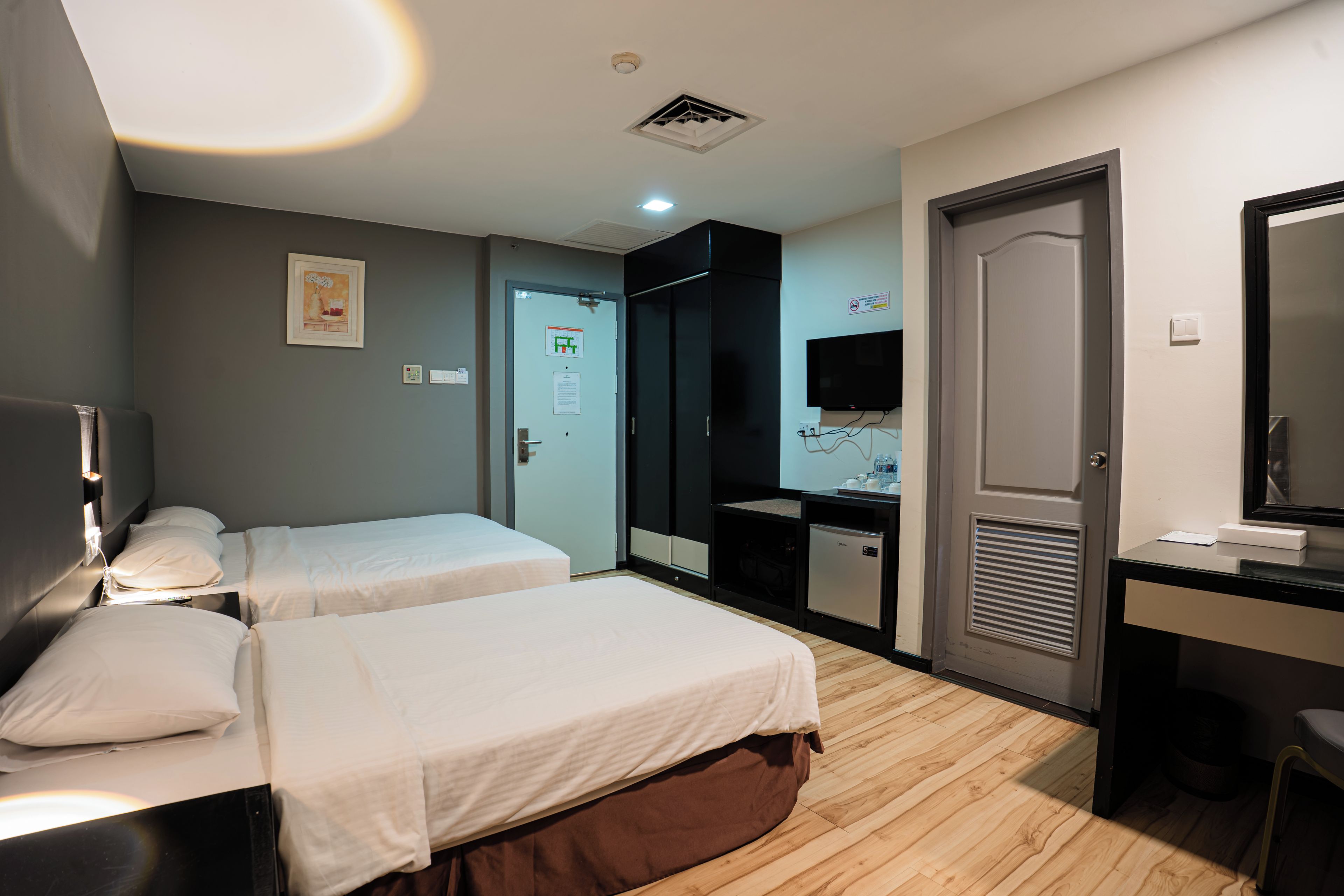 A hotel room with two beds, a desk with a computer, a television, and a door with a sign.