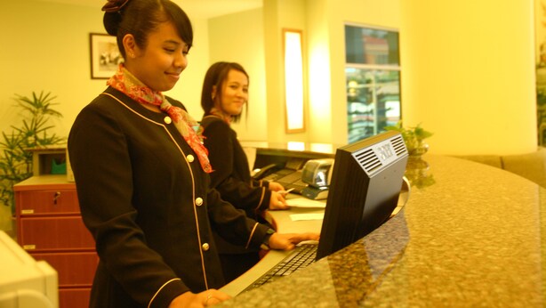 A reception area with a receptionist at a computer, a desk, and a plant. - The Pavilion Hotel (Sandakan)