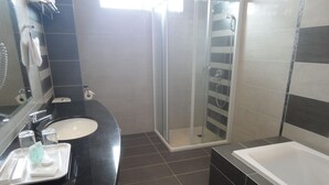 A modern bathroom with a black countertop, a white sink, a glass-enclosed shower, and a separate bathtub.