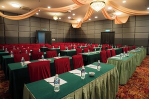 Un salón de conferencias con mesas dispuestas en filas, sillas rojas y manteles verdes.