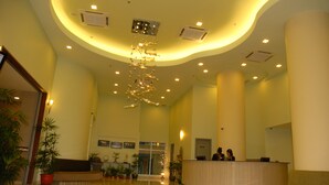 A spacious lobby with a reception desk, potted plants, and a modern ceiling design.