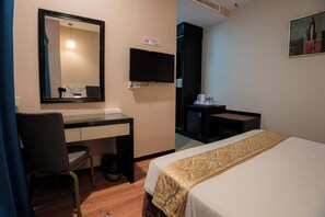 Una habitación de hotel con una cama, un escritorio, una silla, un televisor y una mesita con cafetera.