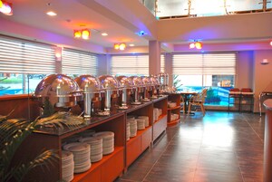 A buffet setup with multiple serving stations, a seating area with chairs, and a view of the outdoors through large windows.