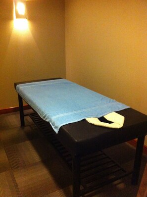 Una cama individual con sábana azul en una habitación con suelo a cuadros y una lámpara de pared.