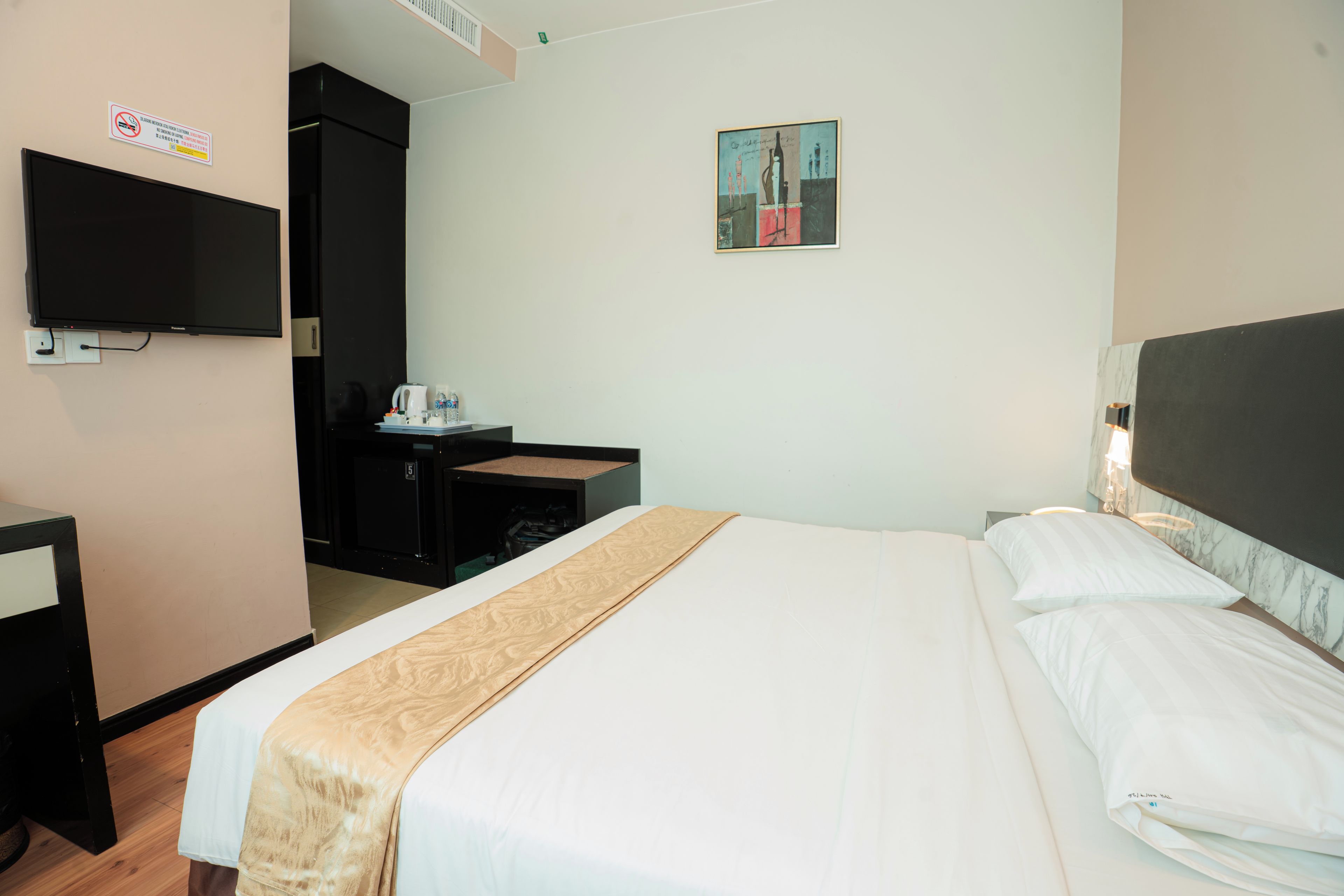 A hotel room with a bed, a desk, a chair, a television, and a painting on the wall.