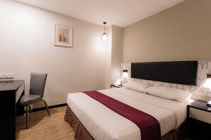 Habitación de hotel con cama, escritorio, silla, mesita de noche y televisor montado en la pared.
