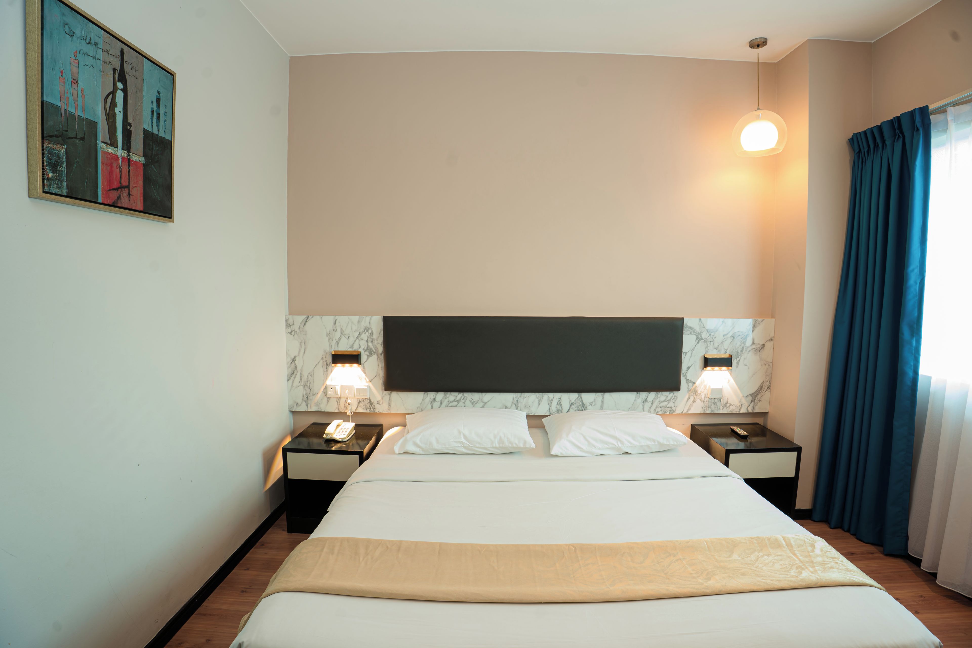 A hotel room with a large bed, two bedside tables with lamps, a marble headboard, and a painting on the wall.