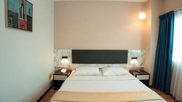A hotel room with a large bed, two bedside tables with lamps, a marble headboard, and a painting on the wall.