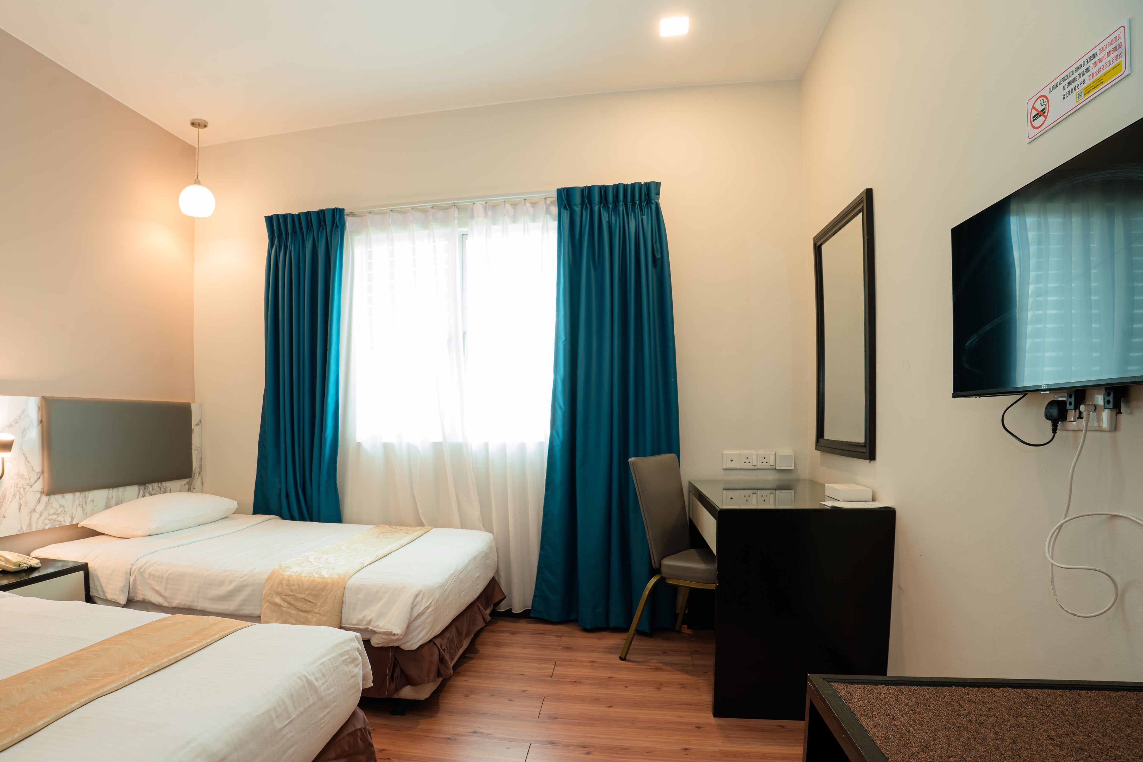 Habitación de hotel con dos camas, un escritorio, una silla, un televisor y una ventana con cortinas.
