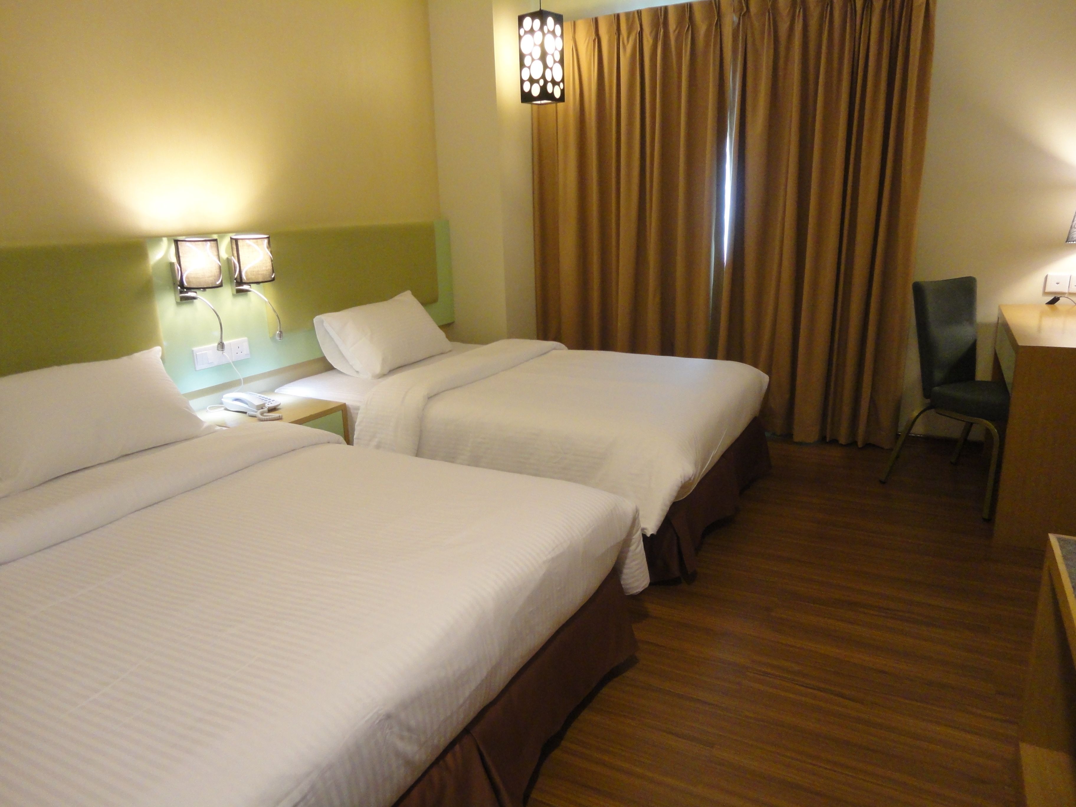 A hotel room with two beds, a desk, a chair, and a window with curtains.