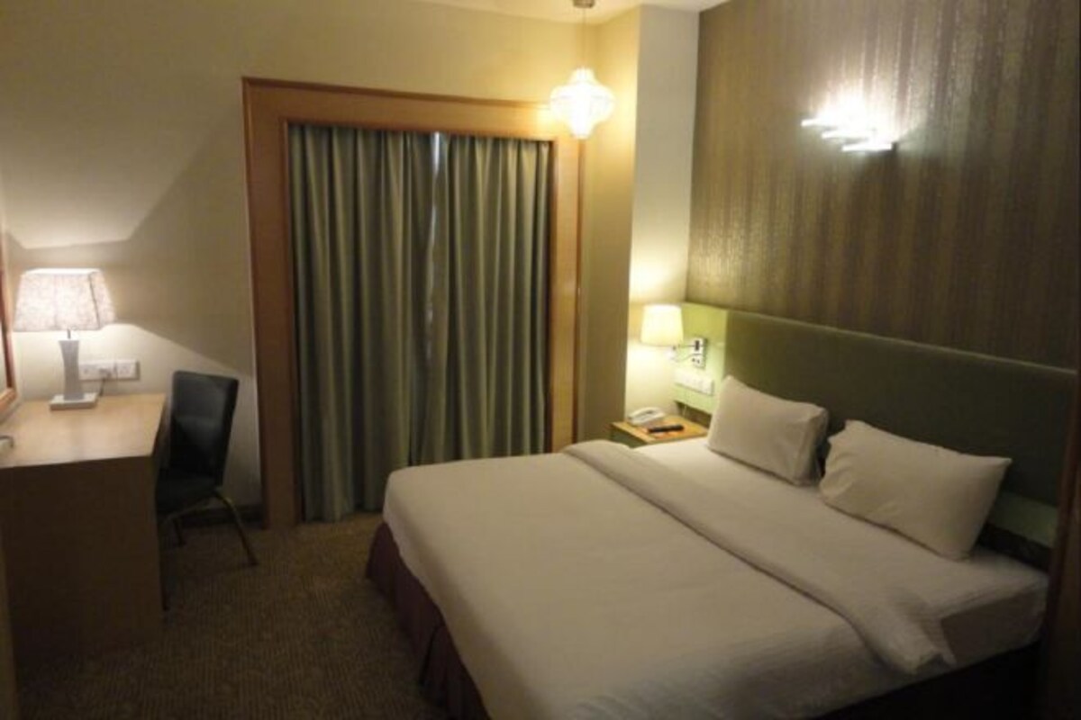 A hotel room with a bed, a desk, a chair, a lamp, and a curtain.