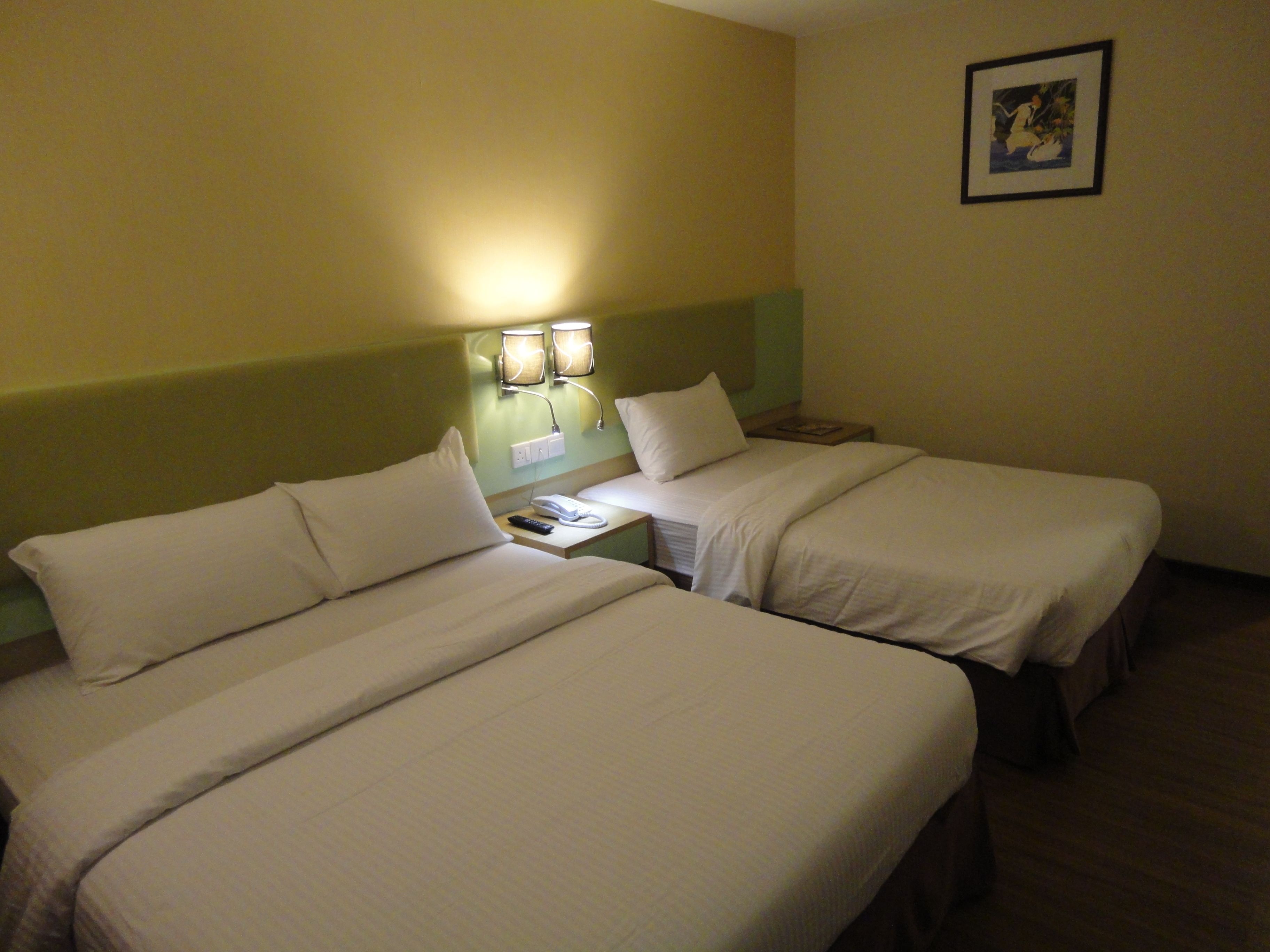 Quarto de hotel com duas camas, uma mesa de cabeceira com abajur e um quadro pendurado na parede.