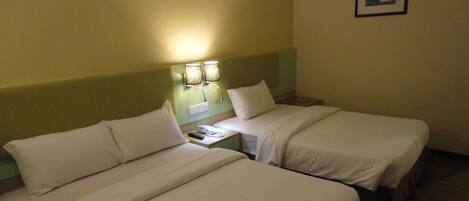 Quarto de hotel com duas camas, uma mesa de cabeceira com abajur e um quadro pendurado na parede.