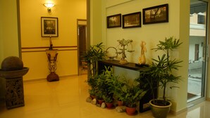 A reception area with a polished floor, a reception desk, potted plants, framed pictures on the wall, and a decorative lamp. - The Pavilion Hotel (Sandakan)