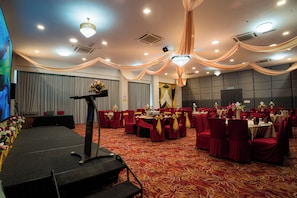 Un salón de banquetes con asientos escalonados, un escenario con un atril y una araña.