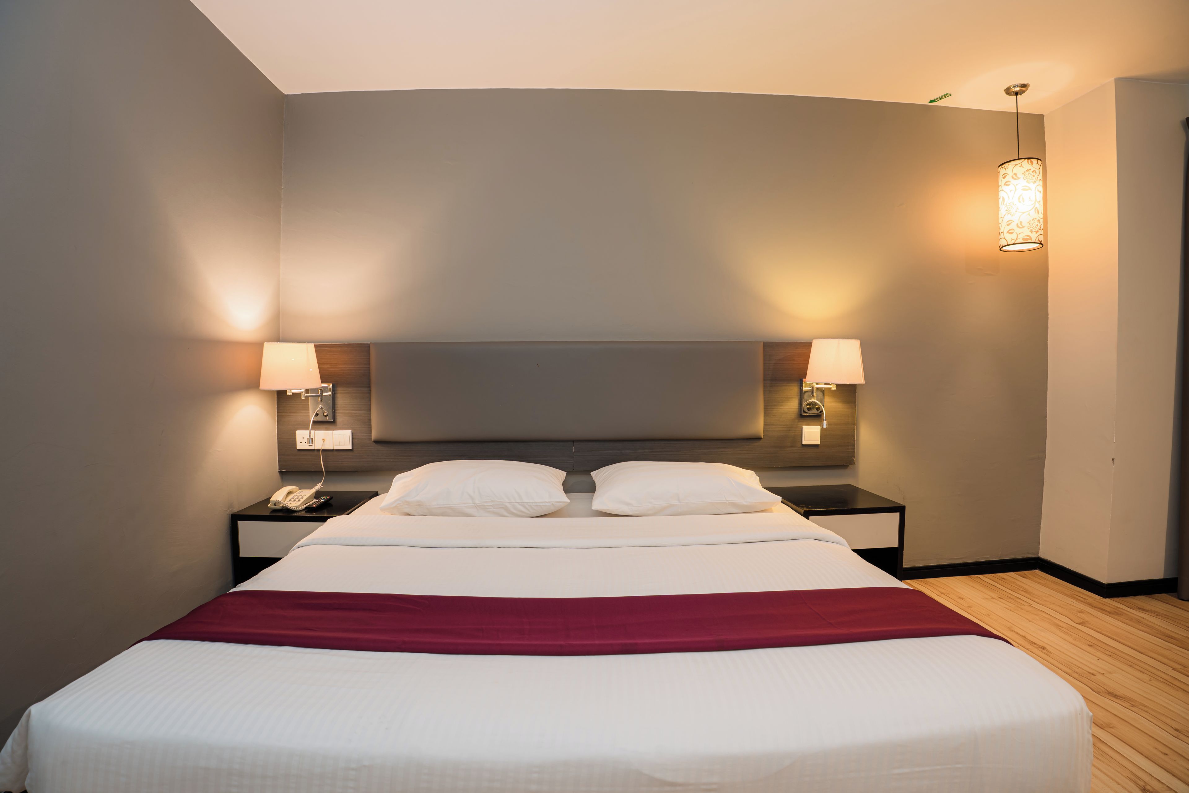 A hotel room with a large bed, two bedside lamps, a telephone, and a red throw blanket.