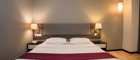 A hotel room with a large bed, two bedside lamps, a telephone, and a red throw blanket.