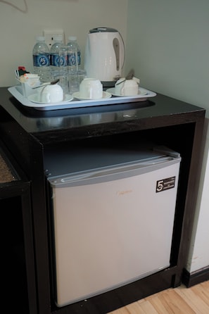 Un minibar compacto con un refrigerador, una cafetera y una bandeja con tazas y una cuchara.
