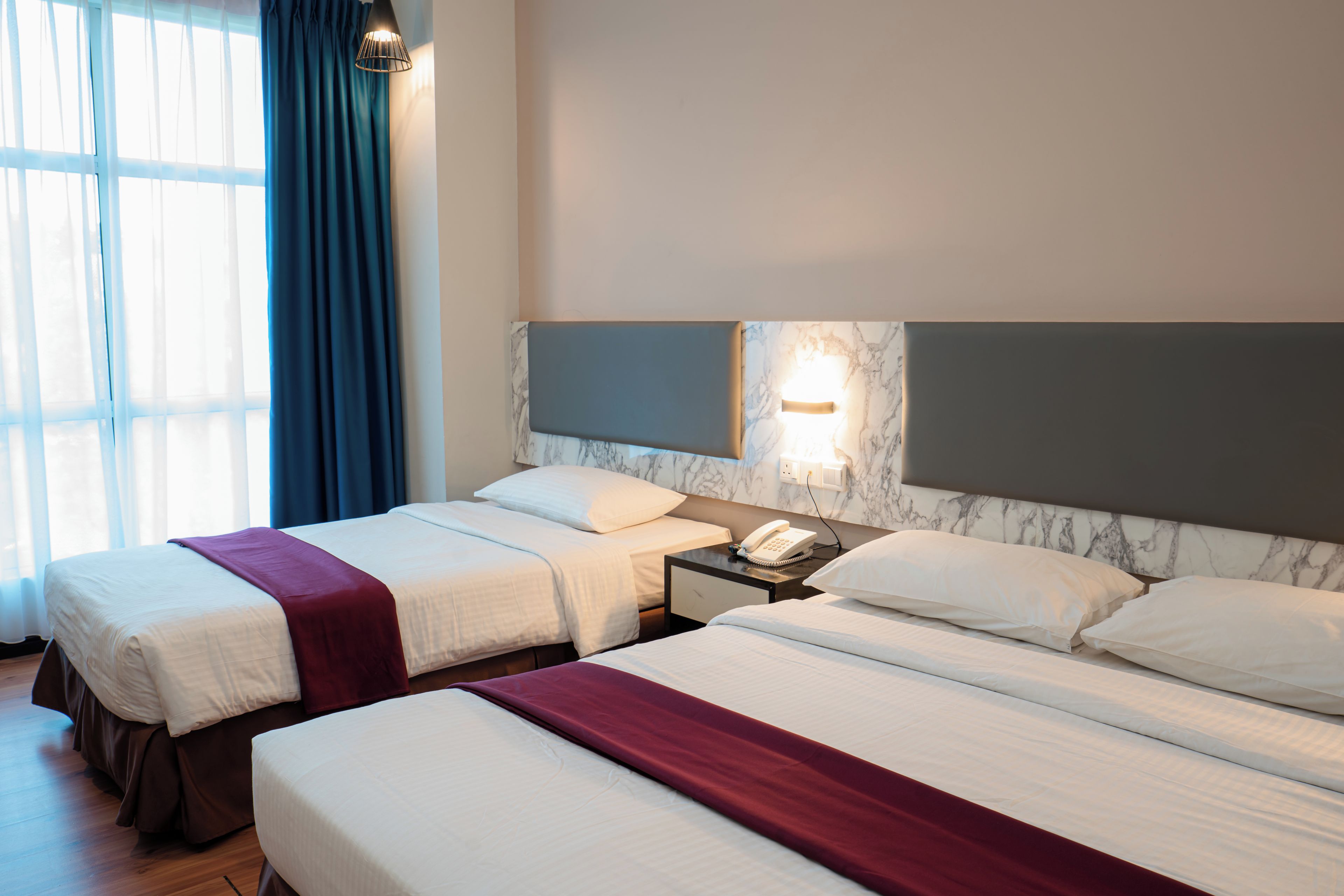 A hotel room with two beds, a nightstand, a telephone, and a window with curtains.