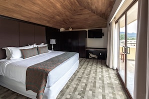 A bedroom with a large bed, a TV mounted on the wall, and a view of the outside through a sliding door.