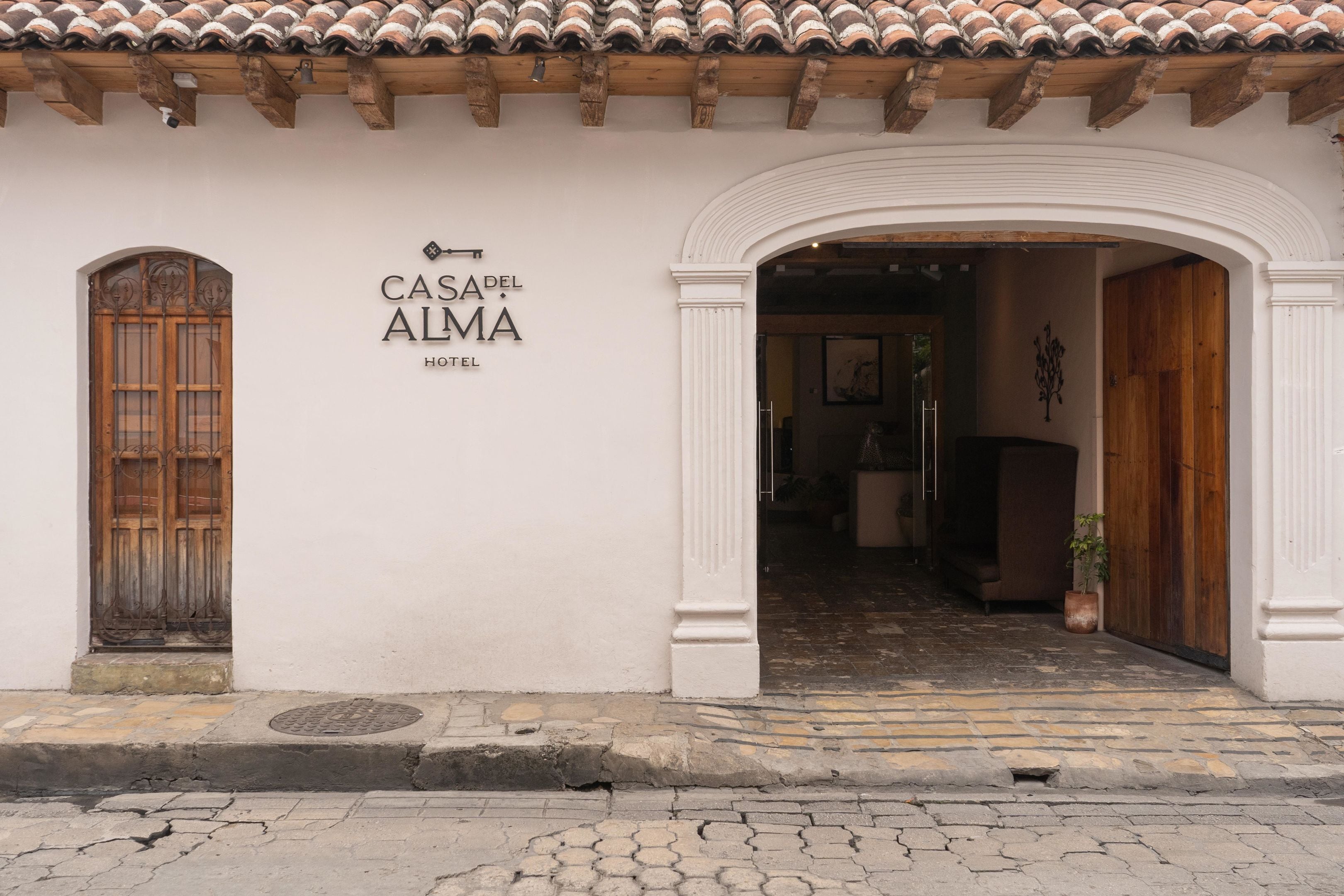 La entrada al Hotel Casa del Alma, con un diseño tradicional que presenta techo de tejas, puertas de madera y un camino de adoquines que conduce a la entrada.