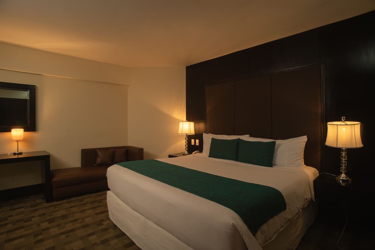 Une chambre d’hôtel avec un grand lit, deux tables de chevet avec des lampes, un petit canapé et un miroir au mur.